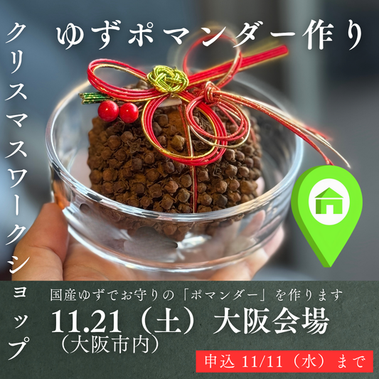 赤い紐と緑の結びが付いた茶色い香り玉（ポマンダー）を手に持つ様子
